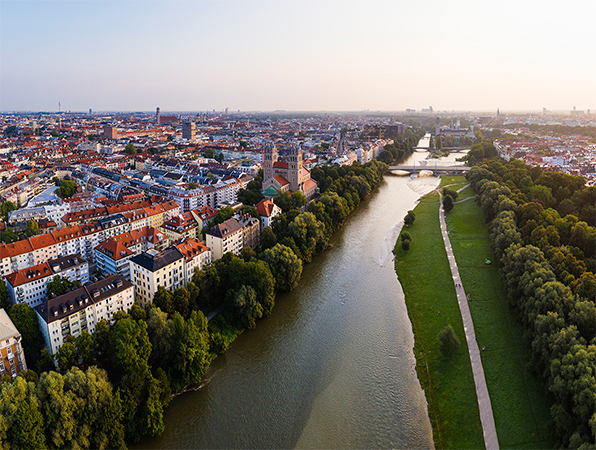 Luftaufnahme von München mit einem Fluss, Bäumen und einem Weg am Fluss entlang.