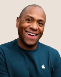 어두운 회색의 짧은 머리에 미소 짓고 있는 Apple Retail 팀원의 인물 사진.