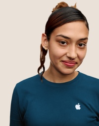분홍색 하이라이트가 들어간 긴 검은 머리에 미소 짓고 있는 Apple Retail 팀원의 인물 사진.