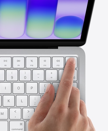 Stříbrný MacBook Neo s prstem na snímači Touch ID v pravém horním rohu klávesnice