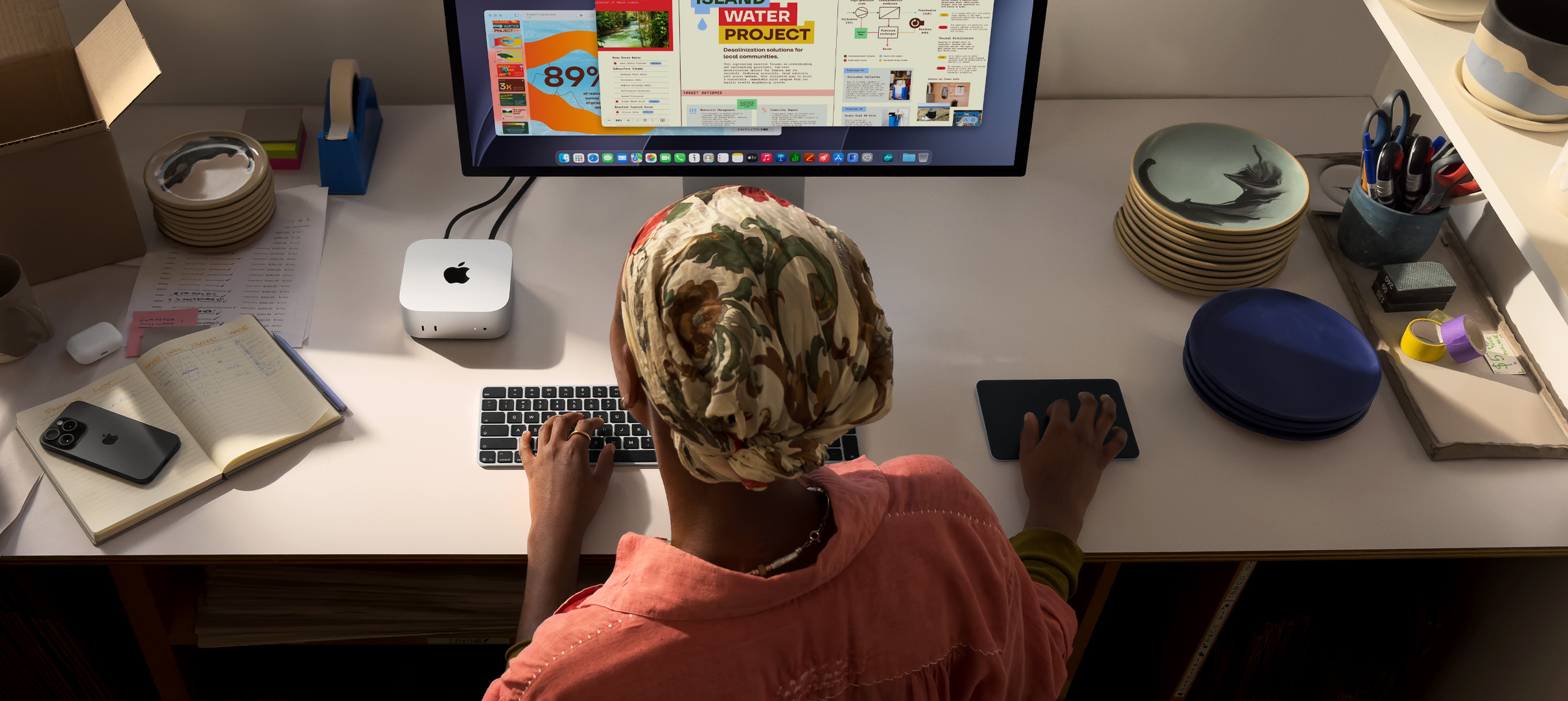 デスクでMac miniを使ってタイピングしている人物。Studio Displayが接続されている。Magic Keyboard、Magic Trackpad、様々なアイテムがある