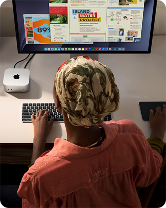 شخص يطبع وهو جالس إلى مكتب مع جهاز Mac mini، شاشة Studio Display متصلة، لوحة مفاتيح ماجيك، لوحة تعقب ماجيك، أغراض متنوعة