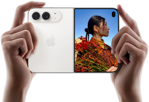iPhone Duo, culoare Alb stelar, ținut de două mâini în dispunere orizontală, desfășurat, partea din stânga prezintă camerele spate Dual Fusion de 48 MP, partea din dreapta prezintă o persoană care se pozează pe ecranul extern, subiectul pozelor poate vedea chipul său în timp ce poza este făcută cu ajutorul aplicației Previzualizare Duo