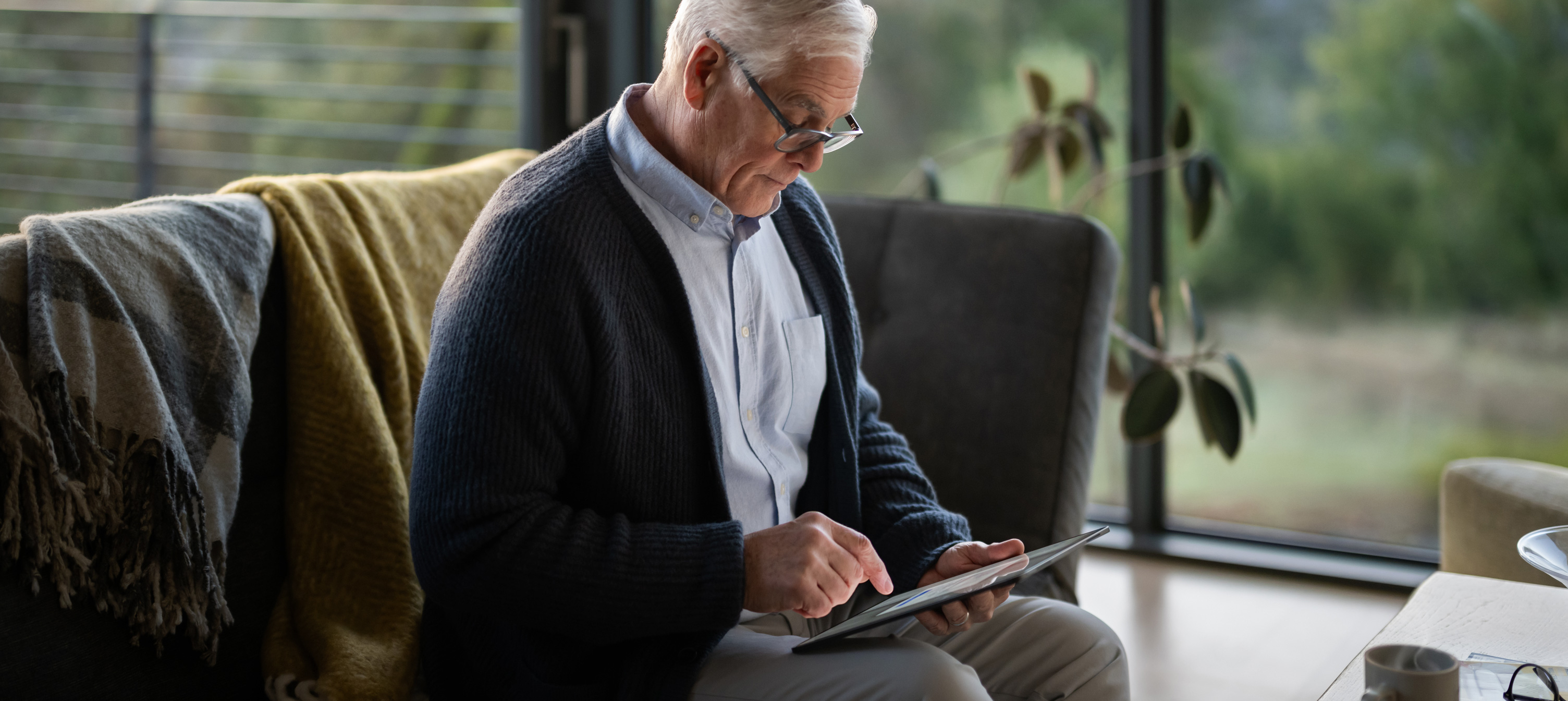 En ældre mand sidder på en sofa og kigger på en iPad.
