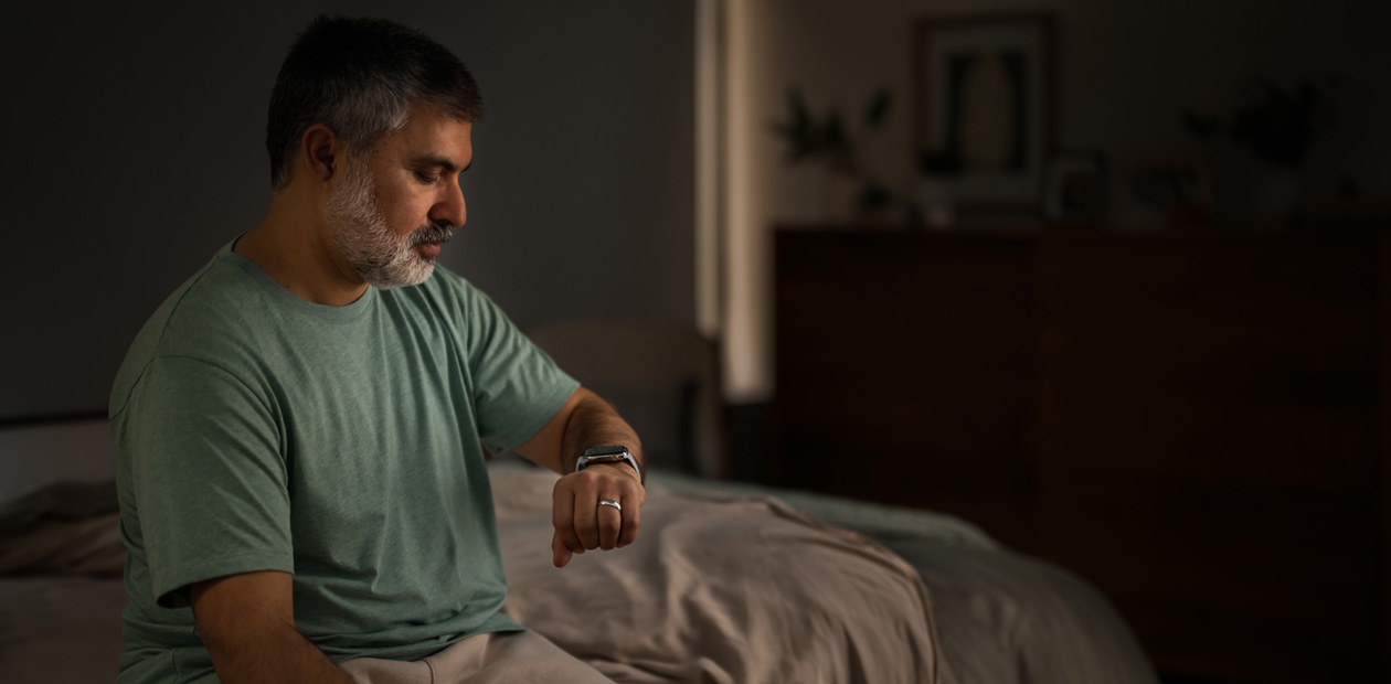 ベッドに座ってApple Watchをチェックする男性
