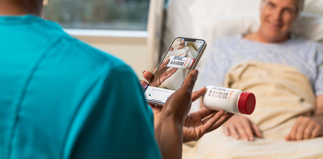A nurse in teal scrubs scans a patient's medicine with her iPhone.
