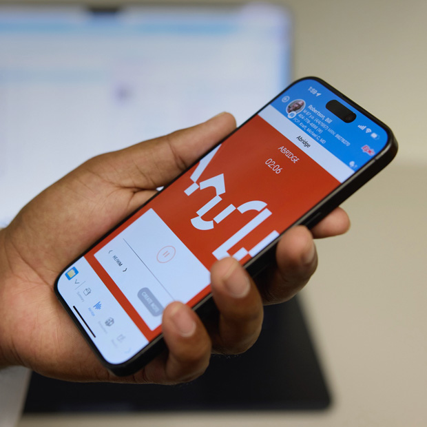 A hand holding an iPhone displaying the Abridge app that translates patient-clinician conversations into clinical notes.