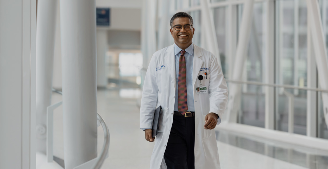 A doctor holding MacBook under their right arm while walking.