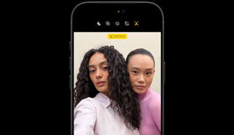 黑色 iPhone 18 Pro，機身正面，使用面孔追蹤功能拍攝兩個人，展示 Center Stage 前置相機功能