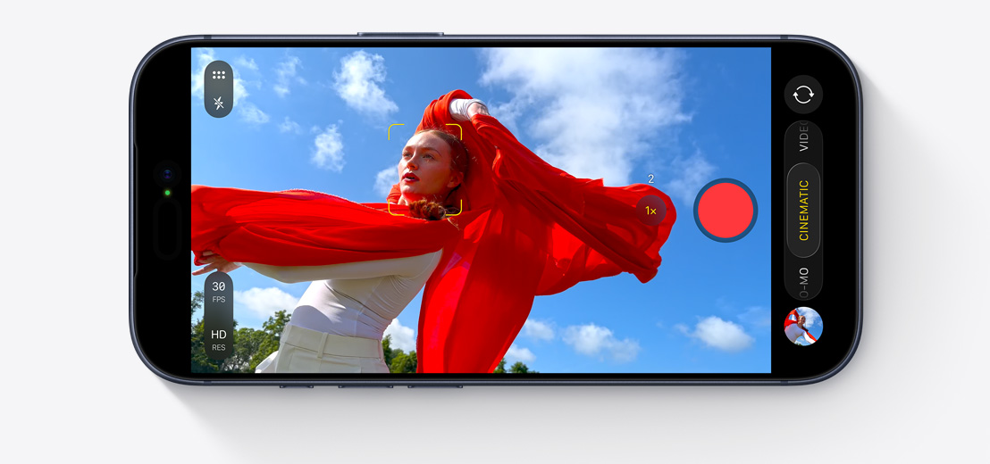 Екран на iPhone с активиран Cinematic Mode, заснема танцуващ човек с развяващ се червен шал на открито