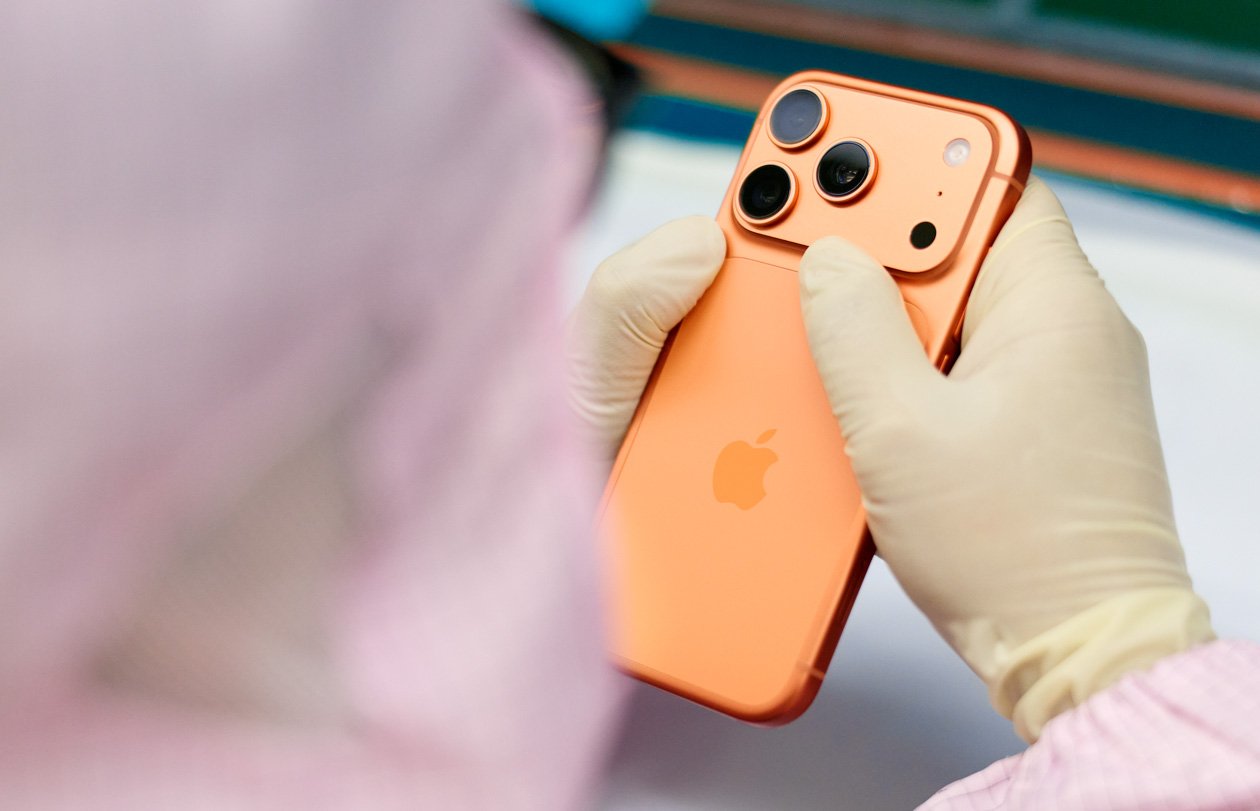 An employee in full-body work suit inspects an iPhone at a work station