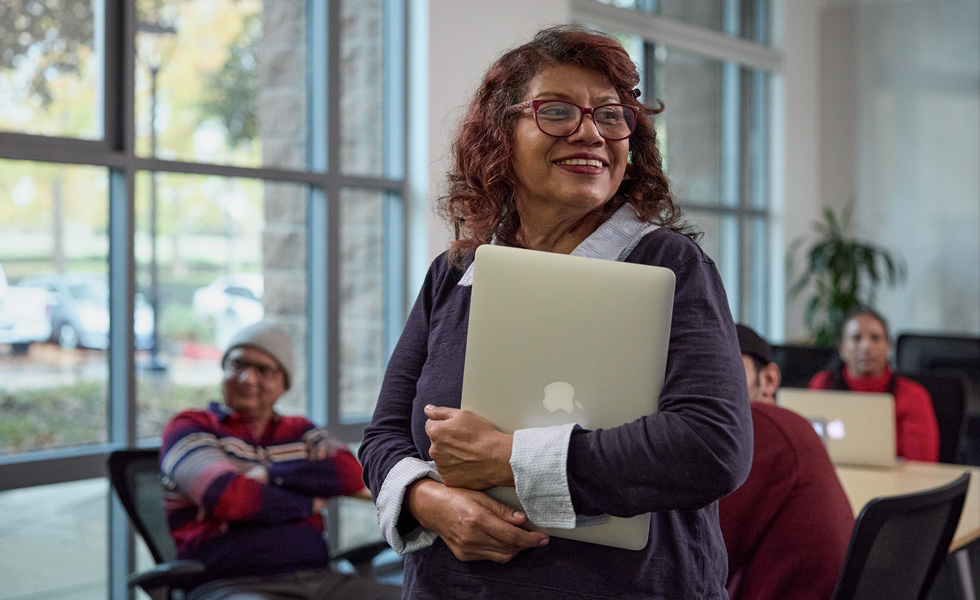 A person carries their laptop in front of a classroom or learning setting
